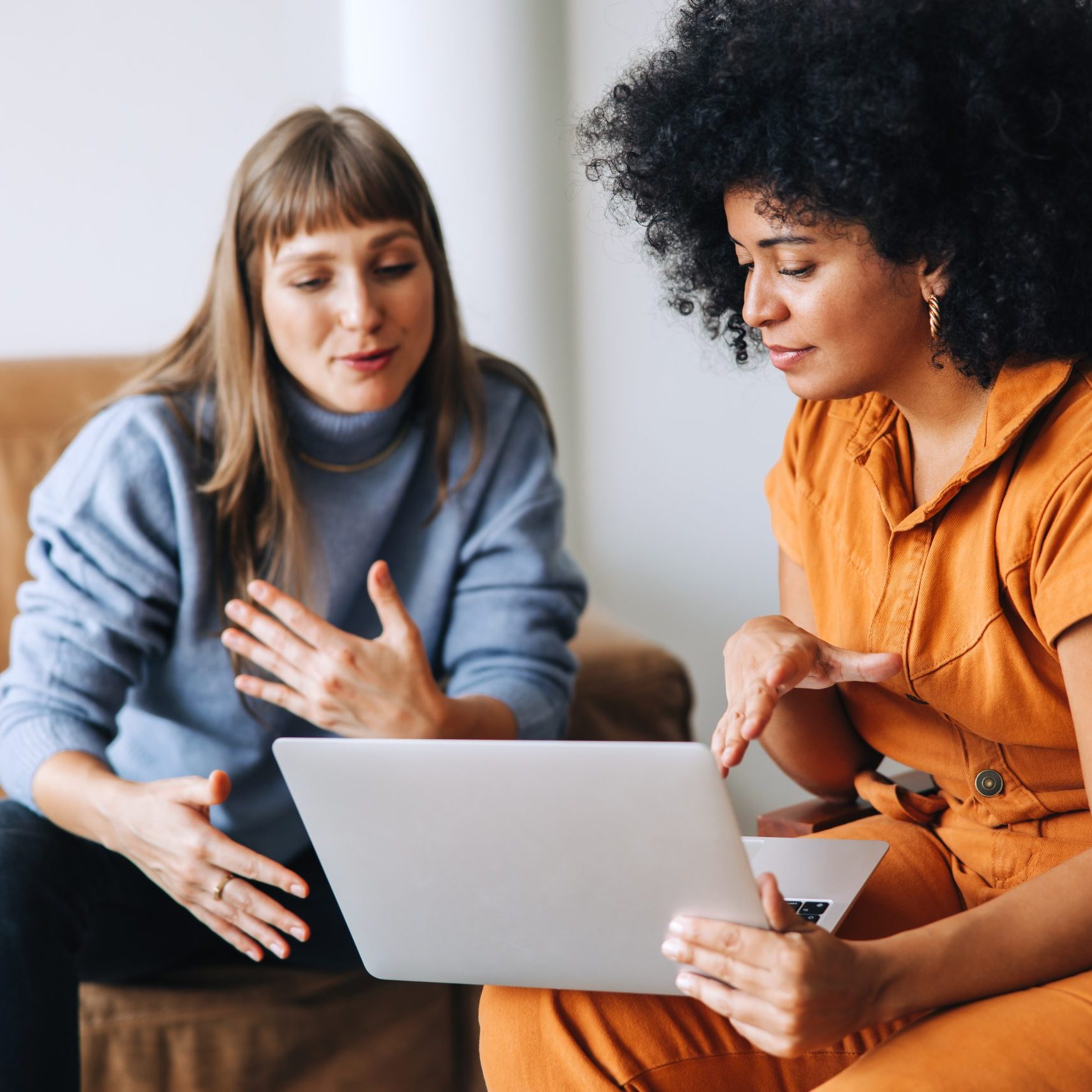 Two young businesswomen having a discussion while looking at a laptop screen. Two female entrepreneurs working as a team in a modern workplace.